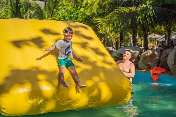 Papá e hijo pasan por una carrera de obstáculos inflable en la piscina — Foto de Stock