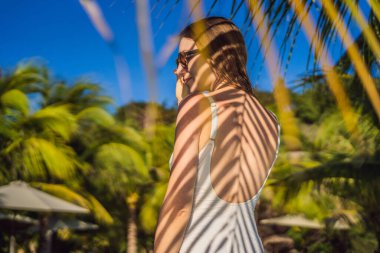 Sırtında palmiye yaprağı gölgesi olan genç bir kadın. Deniz kenarında dinleniyor.