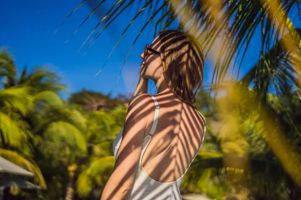 Young woman with the shadow of the palm leaf on her back. Relaxing on the seaside