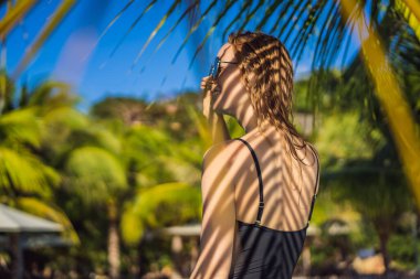 Sırtında palmiye yaprağı gölgesi olan genç bir kadın. Deniz kenarında dinleniyor.