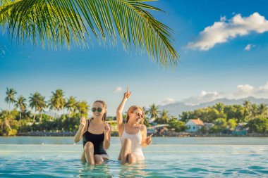 Yaz tatilinde bir tatil köyünün havuzunun havuz kenarında oturan iki güzel genç kadın. Tropikal ülkelerde parti ve turizm