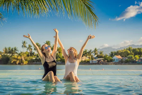 Due belle giovani donne sedute a bordo piscina di una piscina resort durante le vacanze estive. Festa, turismo nei paesi tropicali — Foto Stock