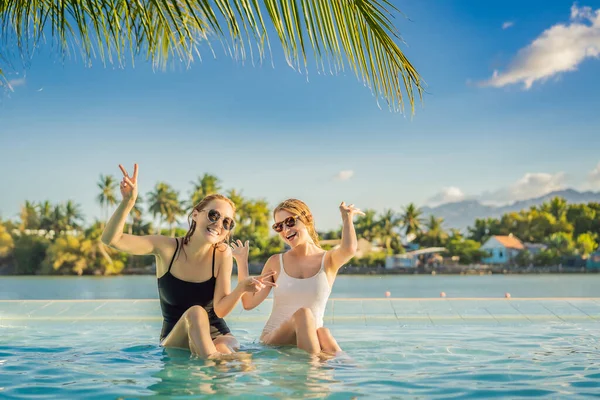 Due belle giovani donne sedute a bordo piscina di una piscina resort durante le vacanze estive. Festa, turismo nei paesi tropicali — Foto Stock