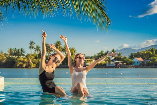 Due belle giovani donne sedute a bordo piscina di una piscina resort durante le vacanze estive. Festa, turismo nei paesi tropicali — Foto Stock