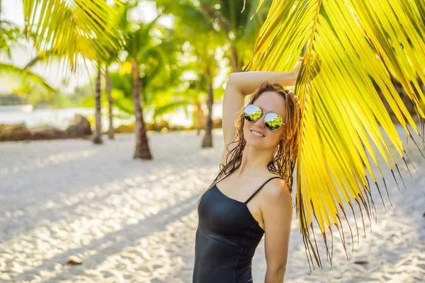 Jovem mulher bonita em maiô na praia tropical, férias de verão, folha de palmeira, pele bronzeada, areia, sorrindo, feliz. Mulher viajante feliz — Fotografia de Stock