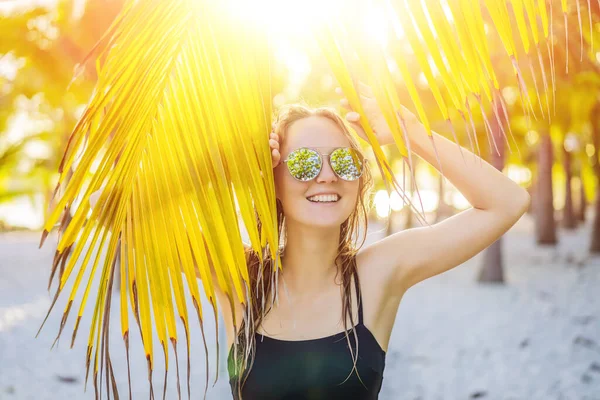 Jovem mulher bonita em maiô na praia tropical, férias de verão, folha de palmeira, pele bronzeada, areia, sorrindo, feliz. Mulher viajante feliz — Fotografia de Stock