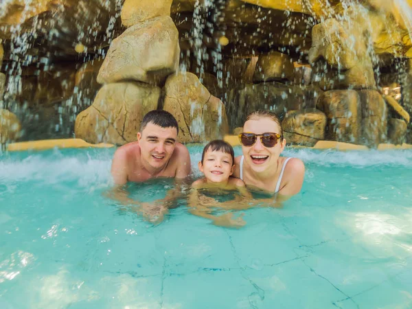 Familia feliz en vacaciones nadando con diversión en la piscina de cascada. Estilo de vida activo, actividades de viajes al aire libre en vacaciones de verano en la isla tropical — Foto de Stock