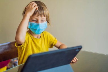 Çocuk evde bir tablet kullanarak online çalışıyor. Annem öğrenmesine yardım ediyor. Koronovirüsten korunmak için maskeli anne ve oğul. Karantina sırasında ders çalışmak. Küresel salgın covid19 virüsü
