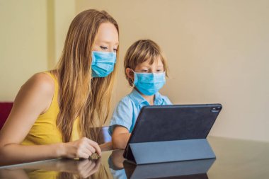 Çocuk evde bir tablet kullanarak online çalışıyor. Annem öğrenmesine yardım ediyor. Koronovirüsten korunmak için maskeli anne ve oğul. Karantina sırasında ders çalışmak. Küresel salgın covid19 virüsü