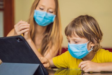 Çocuk evde bir tablet kullanarak online çalışıyor. Annem öğrenmesine yardım ediyor. Koronovirüsten korunmak için maskeli anne ve oğul. Karantina sırasında ders çalışmak. Küresel salgın covid19 virüsü