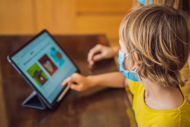 Çocuk evde bir tablet kullanarak online çalışıyor. Annem öğrenmesine yardım ediyor. Koronovirüsten korunmak için maskeli anne ve oğul. Karantina sırasında ders çalışmak. Küresel salgın covid19 virüsü
