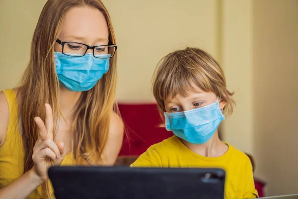 Chłopiec uczy się online w domu za pomocą tabletu. Mama pomaga mu się uczyć. Mama i syn w maskach medycznych do ochrony przed koronowirusem. Uczę się podczas kwarantanny. Globalny wirus pandemii19 — Zdjęcie stockowe