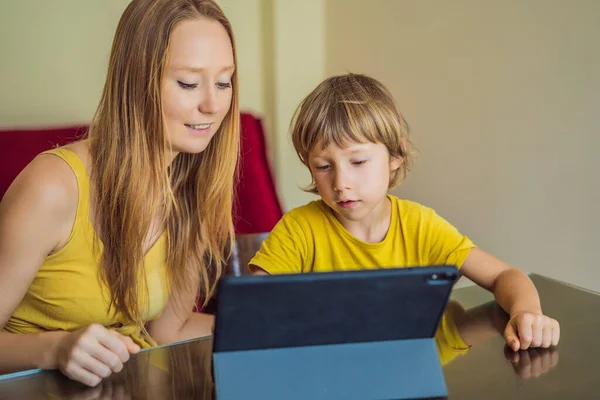 Un chico que estudia en línea en casa usando una tableta. Mamá le ayuda a aprender. Estudiar durante la cuarentena. Virus covidémico pandémico global19 — Foto de Stock