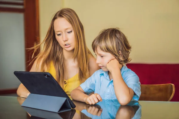Un chico que estudia en línea en casa usando una tableta. Mamá le ayuda a aprender. Estudiar durante la cuarentena. Virus covidémico pandémico global19 — Foto de Stock