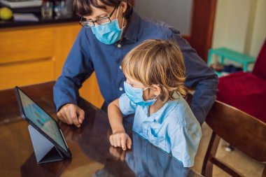 Çocuk evde bir tablet kullanarak online çalışıyor. Babam öğrenmesine yardım ediyor. Koronovirüsten korunmak için maskeli baba ve oğul. Karantina sırasında ders çalışmak. Küresel salgın covid19 virüsü