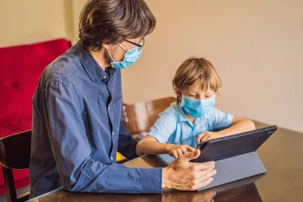 Boy studying online at home using a tablet. Father helps him learn. Father and son in medical masks to protect against coronovirus. Studying during quarantine. Global pandemic covid19 virus — Stock Photo, Image
