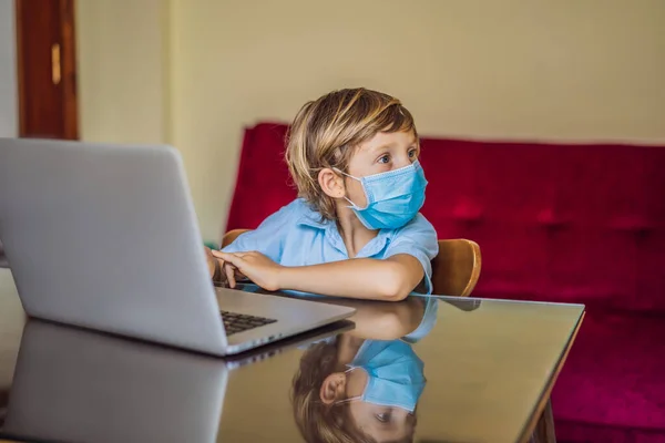 Niño estudiando en línea en casa con el uso de ordenador portátil en máscaras médicas para proteger contra el coronovirus. Estudiar durante la cuarentena. Virus covidémico pandémico global19 — Foto de Stock