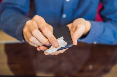 Adam akıllı telefon ekranını alkol veya dezenfektanla temizliyor. Hastalıkları önlemek için kirli ekranlı telefonu temizleme kavramı. Coronavirus covid 19