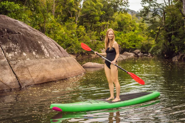 SUP Stand Up Paddle Board Frau paddelt auf dem See stehend glücklich auf dem Tretbrett auf blauem Wasser. Action Shot von junger Frau auf Paddelbrett — Stockfoto