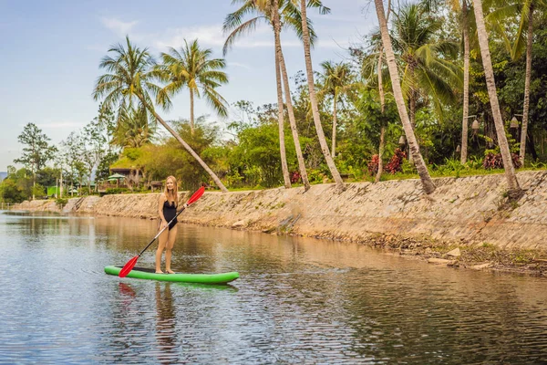 SUP Stand Up Paddle Board Frau paddelt auf dem See stehend glücklich auf dem Tretbrett auf blauem Wasser. Action Shot von junger Frau auf Paddelbrett — Stockfoto