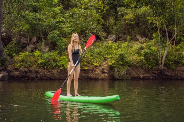 SUP Levante-se paddle board mulher paddle embarque no lago de pé feliz em paddleboard em água azul. Ação tiro de jovem mulher no tabuleiro de remo — Fotografia de Stock