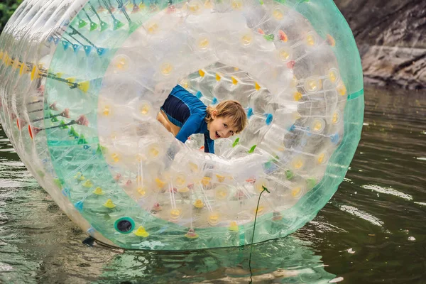 Милый маленький мальчик, играет в Зорб катящегося пластикового кольца цилиндра с отверстием в середине на озере — стоковое фото