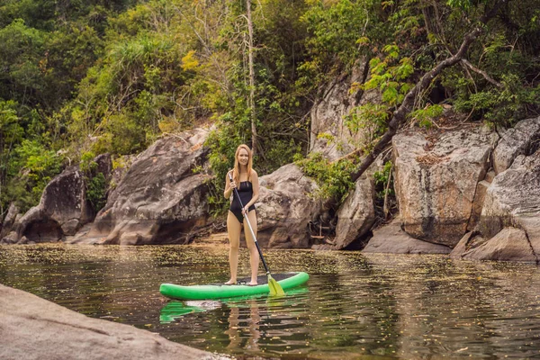 SUP Stand up κουπί του σκάφους γυναίκα κουπί επιβίβασης στη λίμνη στέκεται ευτυχισμένη στο paddleboard σε μπλε νερό. Δράση Shot of Young Woman on Paddle σκάφους — Φωτογραφία Αρχείου