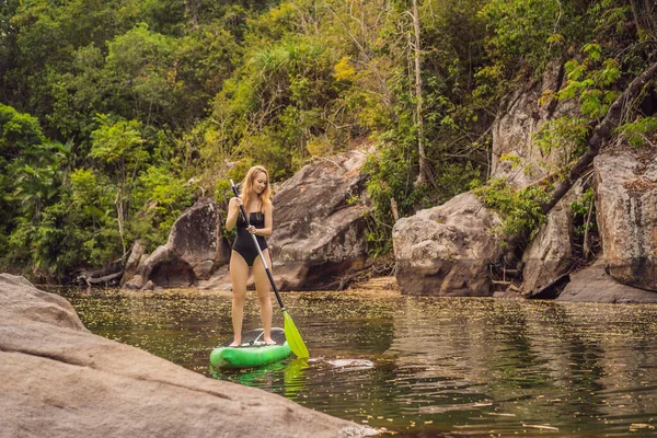 SUP Wstań paddle board kobieta paddle boarding na jeziorze stoi szczęśliwy na paddleboard na niebieskiej wodzie. Akcja Shot młodej kobiety na tablicy Paddle — Zdjęcie stockowe