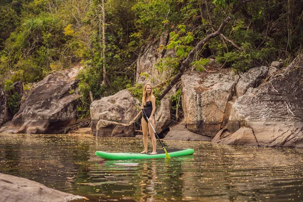 苏打水站起来划桨板女人划桨板在湖上站着高兴地在蓝水划桨板上。青年女子在垫板上的动作镜头 — 图库照片