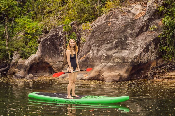 SUP Stand Up Paddle Board Frau paddelt auf dem See stehend glücklich auf dem Tretbrett auf blauem Wasser. Action Shot von junger Frau auf Paddelbrett — Stockfoto