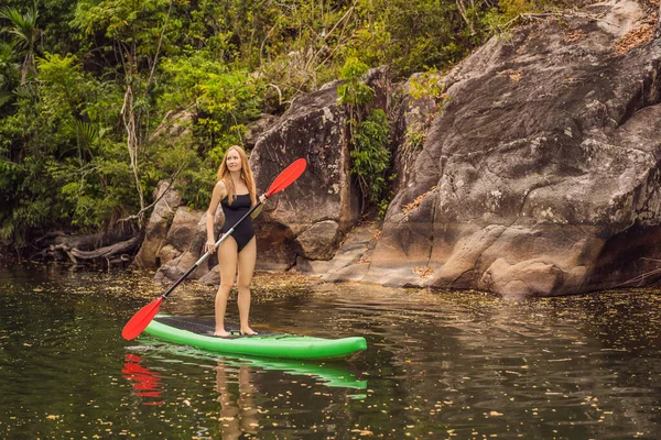 SUP Stå upp paddla ombord kvinna paddla ombordstigning på sjön står glad på paddelbräda på blått vatten. Action Skott av ung kvinna på paddelbräda — Stockfoto