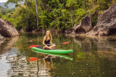 Kalk ayağa kürek çeken kadın gölde kürek çekiyor mavi suda kürek çekerken mutlu duruyor. Genç Kadın Kürek Çekme Kurulu 'nda