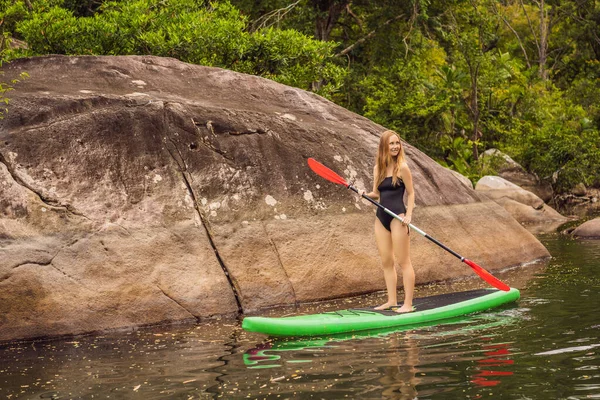 SUP Stå upp paddla ombord kvinna paddla ombordstigning på sjön står glad på paddelbräda på blått vatten. Action Skott av ung kvinna på paddelbräda — Stockfoto