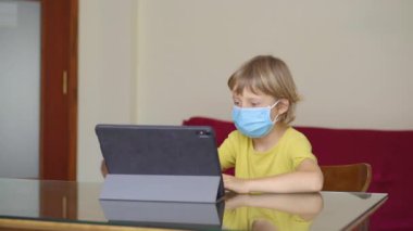 Genç bir kadın ve küçük oğlu karantina sırasında bir evde oturup internet okulunda tablet kullanarak okuyorlar. Corona virüsü konsepti