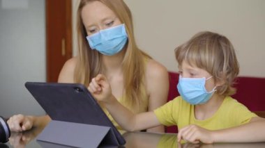Genç bir kadın ve küçük oğlu karantina sırasında bir evde oturup internet okulunda tablet kullanarak okuyorlar. Corona virüsü konsepti