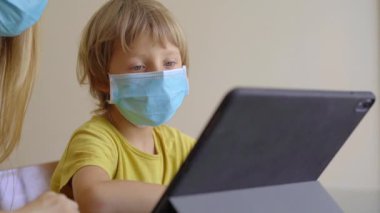 Genç bir kadın ve küçük oğlu karantina sırasında bir evde oturup internet okulunda tablet kullanarak okuyorlar. Corona virüsü konsepti
