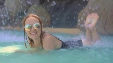 Sıcak pınarları, şelaleleri ve sıcak maden suyu olan yüzme havuzları olan tropikal bir tatil köyünde genç bir kadın.