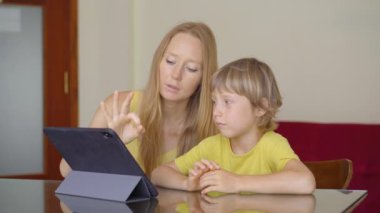 Genç bir kadın ve küçük oğlu karantina sırasında bir evde oturup internet okulunda tablet kullanarak okuyorlar. Corona virüsü konsepti
