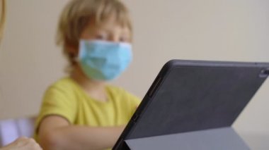 Genç bir kadın ve küçük oğlu karantina sırasında bir evde oturup internet okulunda tablet kullanarak okuyorlar. Corona virüsü konsepti