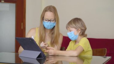 Genç bir kadın ve küçük oğlu karantina sırasında bir evde oturup internet okulunda tablet kullanarak okuyorlar. Corona virüsü konsepti