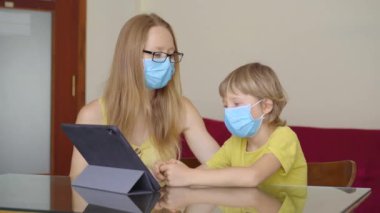 Genç bir kadın ve küçük oğlu karantina sırasında bir evde oturup internet okulunda tablet kullanarak okuyorlar. Corona virüsü konsepti