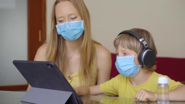 Eine junge Frau und ihr kleiner Sohn sitzen während der Quarantäne zu Hause und lernen mit einem Tablet in der Internetschule. Coronavirus-Konzept — Stockvideo