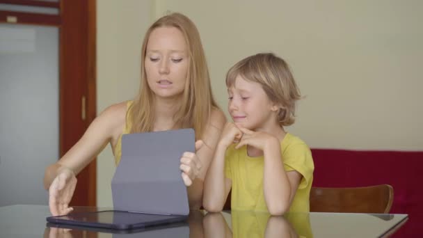 Una giovane donna e il suo piccolo figlio siedono in una casa durante la quarantena e studiano nella scuola di internet usando un tablet. Concetto di virus Corona — Video Stock