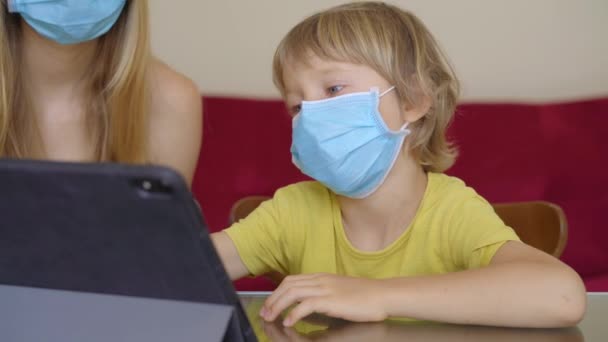 Una mujer joven y su pequeño hijo se sientan en una casa durante la cuarentena y estudian en la escuela de Internet usando una tableta. Concepto de virus Corona — Vídeo de stock