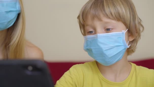 Une jeune femme et son petit fils sont assis dans une maison pendant la quarantaine et étudient à l'école Internet à l'aide d'une tablette. Concept du virus Corona — Video