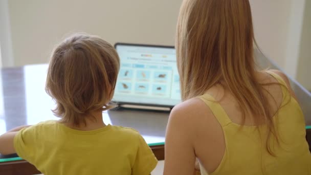 Eine junge Frau und ihr kleiner Sohn sitzen während der Quarantäne zu Hause und lernen mit einem Tablet in der Internetschule. Coronavirus-Konzept — Stockvideo