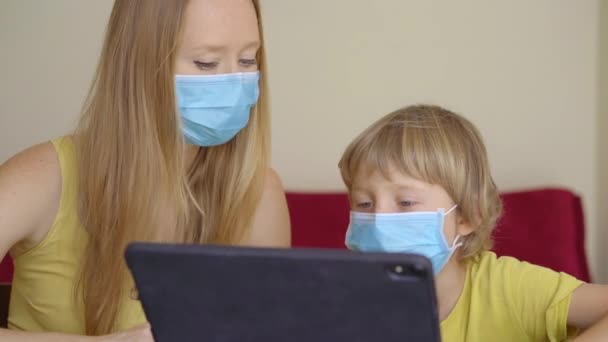 Genç bir kadın ve küçük oğlu karantina sırasında bir evde oturup internet okulunda tablet kullanarak okuyorlar. Corona virüsü konsepti — Stok video