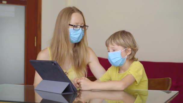 Una giovane donna e il suo piccolo figlio siedono in una casa durante la quarantena e studiano nella scuola di internet usando un tablet. Concetto di virus Corona — Video Stock
