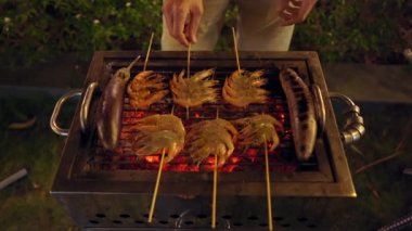 Gece barbekü. Adam ızgarada karides ve sebze pişiriyor.