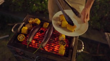 Gece barbekü. Adam ızgarada sebze pişiriyor.